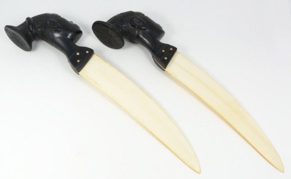 PAIR AFRICAN CARVED IVORY AND EBONY KNIVES: Two hand carved ebony African heads mounted on conforming ivory knife blades. Measures: 15 ½” Length x 3 ½” Width ( 38.1 cm x 8.89 cm).