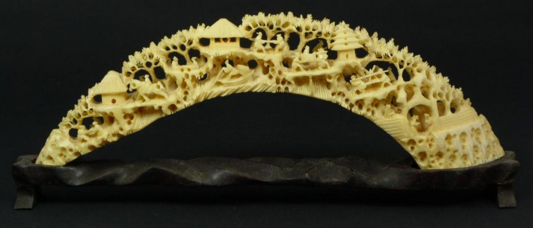 CHINESE PIERCED HAND CARVED IVORY BRIDGE: Antique Chinese fully relief carved ivory tusk depicting village scene with people, horses, boats, pagodas, trees, rock formations and city wall. Includes fitted wooden base. 19th century. Measures ap
