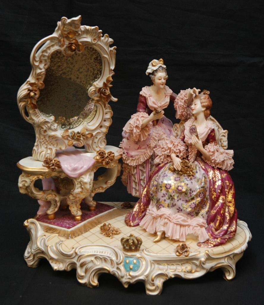 VOLKSTADT GERMAN PORCELAIN GROUP OF WOMEN: A Volkstedt German porcelain group figure depicting two grooming women near a vanity table with mirror. Each having pink lace porcelin designs to dress. Floral hand painted designs throughout dress. S