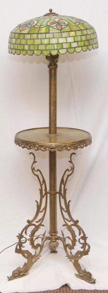 A BRASS & ONYX FLOOR LAMP w SLAG GLASS SHADE: An old brass and onyx floor lamp having a side table design with attached lamp over onyx table top. Scrolled design throughout. Slag glass shade with green and multicolor design. Three feet with figur