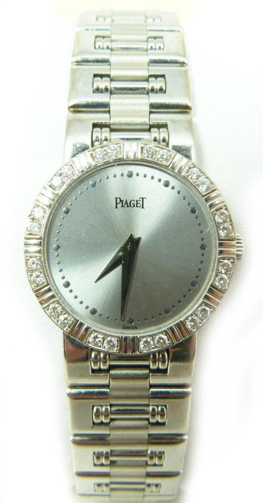PIAGET 18K WHITE GOLD WRISTWATCH w DIAMOND BEZEL: A beautiful ladies Piaget 18k white gold 'Dancer' wrist watch with diamond bezel. Has white gold tone face with beaded notches. Has white gold hour and minute hands. Holds 24 round cut diamonds to bez