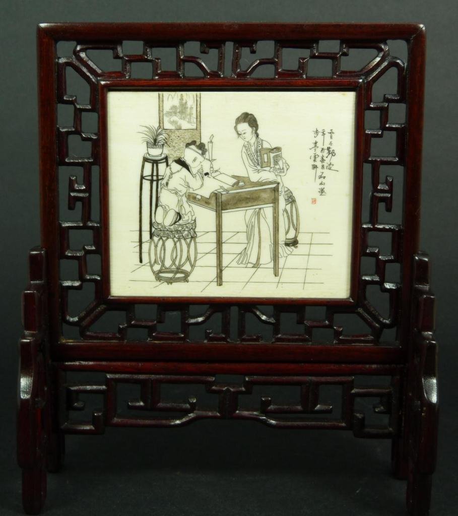 A CHINESE ETCHED IVORY TABLE SCREEN: A Chinese finely etched ivory table screen depicting a mother watching her son as he does his studies. Has calligraphy poem to right hand side and signed with one red etched seal. Set in reticulated t