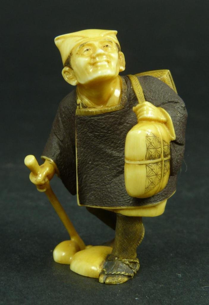 FINE JAPANESE CARVED IVORY NETSUKE SIGNED KOYU: A fine Japanese carved ivory netsuke depicting a traveling retired master. Signed Kuyo to bottom. Includes wooden presentation box. Circa 1965-1970. Amazingly carved and painted. Measures 2" height (5