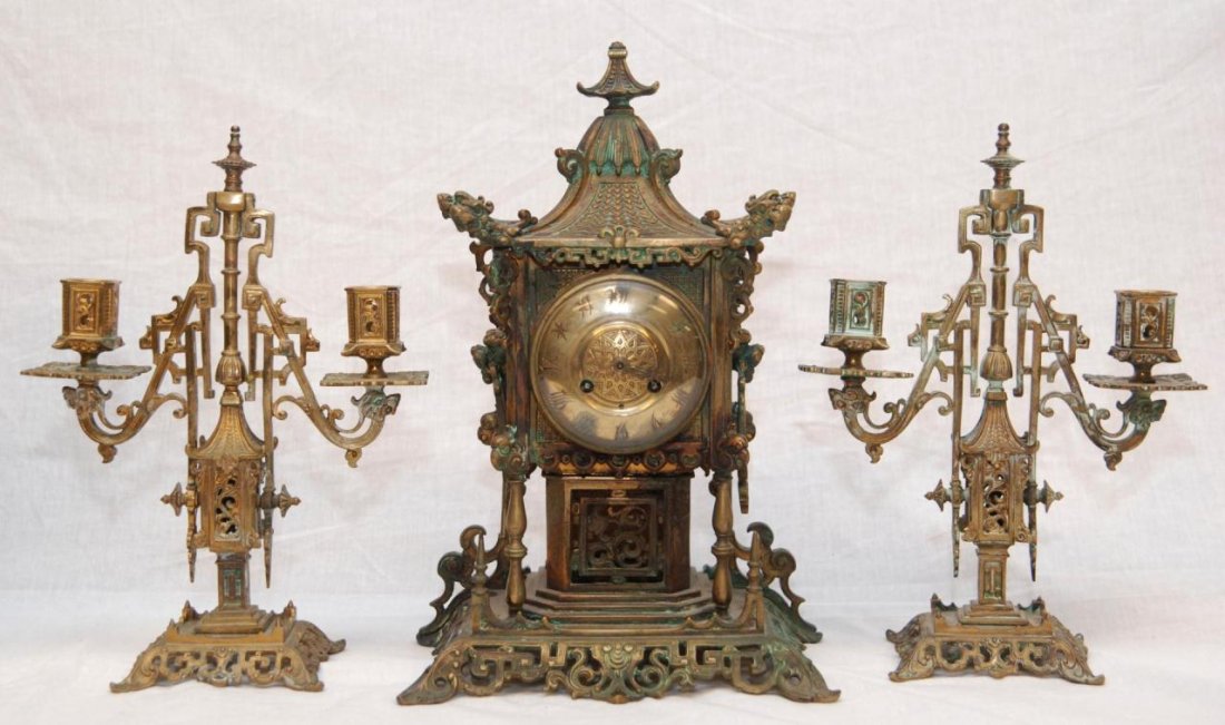 TIFFANY & CO ORIENTAL MOTIF GARNITURE CLOCK SET: A stunning Tiffany & Company gilded bronze garniture clock set having an oriental motif to each piece. Clock has pagoda design with gold face and calligraphy numbers. Figural foo dog head handles to s