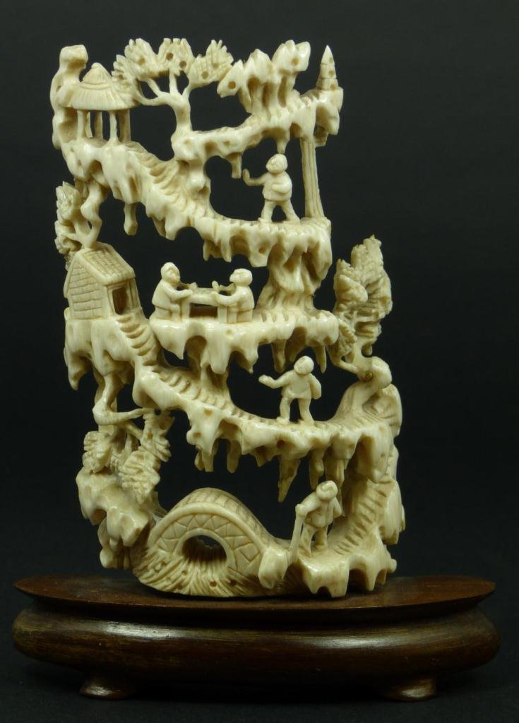 CHINESE CARVED IVORY OPEN WORK VILLAGE PLAQUE: An antique Chinese fully reticulated carved ivory open work village scene plaque. Depicts people, trails, trees, pagodas, men playing games of go, rock formations, bridge and flowing water. Mounted on