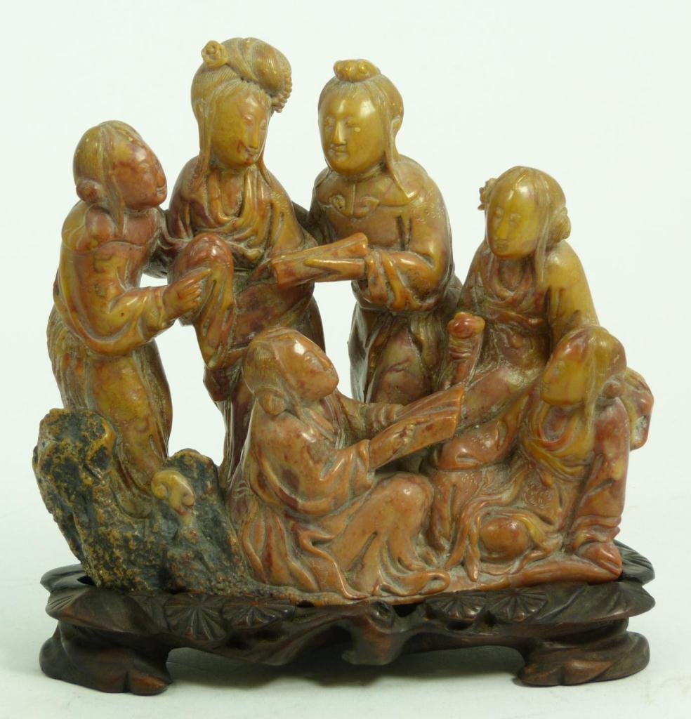 A CHINESE CARVED SOAPSTONE GROUP FIGURE: A Chinese fully relief carved soapstone group figure depicting 6 maidens reading scrolls. One is holding a lingzhi scepter. Includes fitted wooden base. Measures 5 1/4" height x 6 1/4" width + 3/4" ba