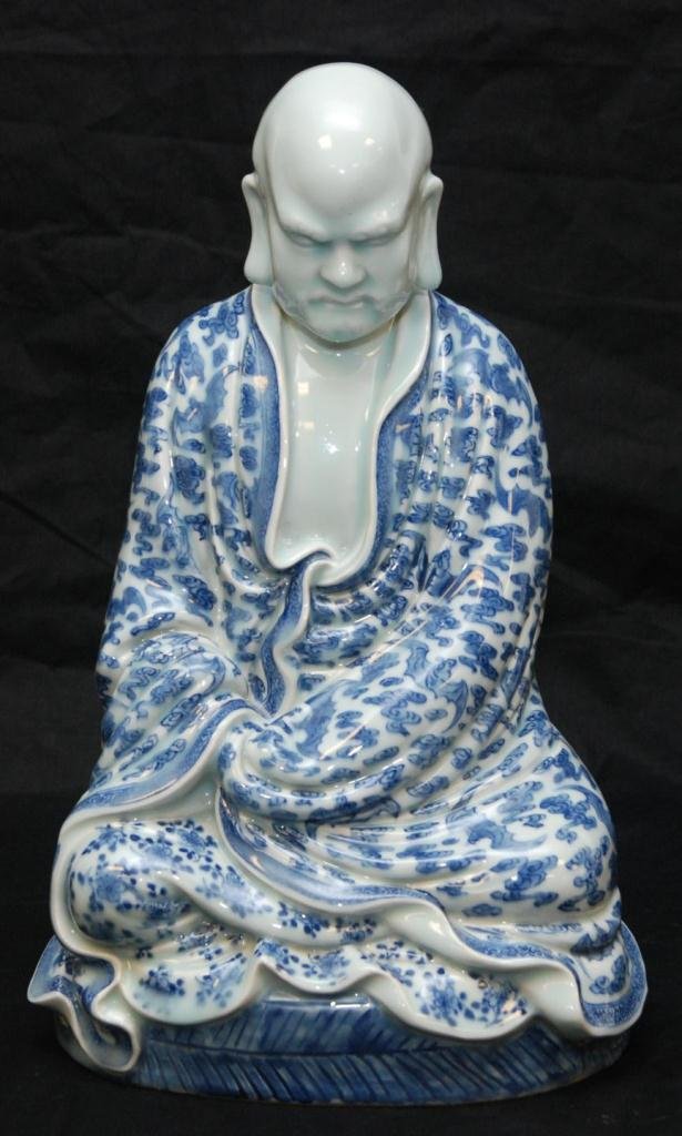 CHINESE BLUE & WHITE PORCELAIN MEDITATING FIGURE: Chinese hand painted blue and white porcelain figure depicting a man seated and meditating with eyes closed. His robe depicts bats flying amongst clouds. Back of base holds Ming Dynasty Wanli reign ma