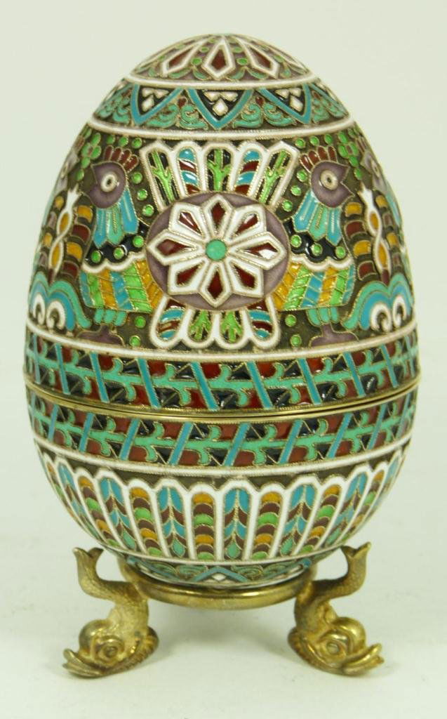 RUSSIAN SILVER ENAMELED EGG: Russian silver enameled egg box having elegant scrolled design with chickens and raised pinwheels. Gold wash interior. Includes stand with three figural fish feet. Piece holds Cyrillic Pavel Akimov Ov