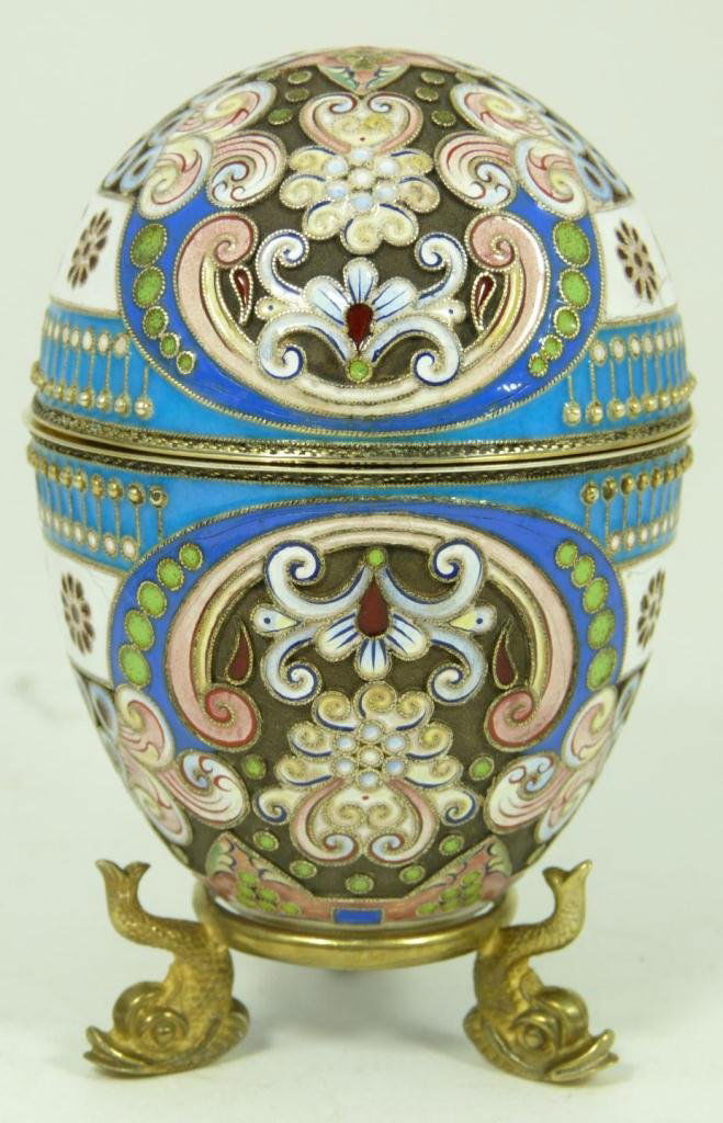 RUSSIAN SILVER ENAMELED EGG ON STAND: Russian silver enameled egg box having elegant multicolor design with B monogram. Gold wash interior. Includes stand with three figural fish feet. Piece holds Cyrillic with double headed eagle marks.