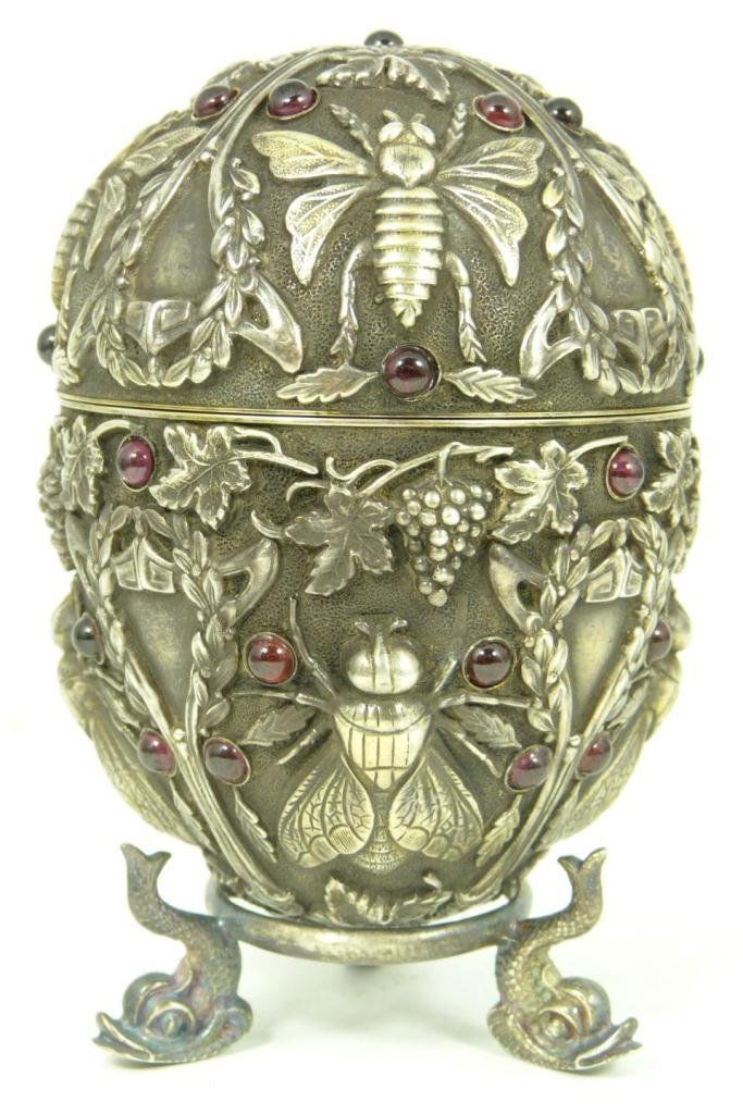 RUSSIAN SILVER FLIES EGG w GARNET AND STAND: Russian silver egg. Has intricate raised design depicting flies, wreaths and grape clusters. Mounted with Cabochon garnets throughout. Gold wash interior. Has Pavel Ovchinnikov workmaster marks to int