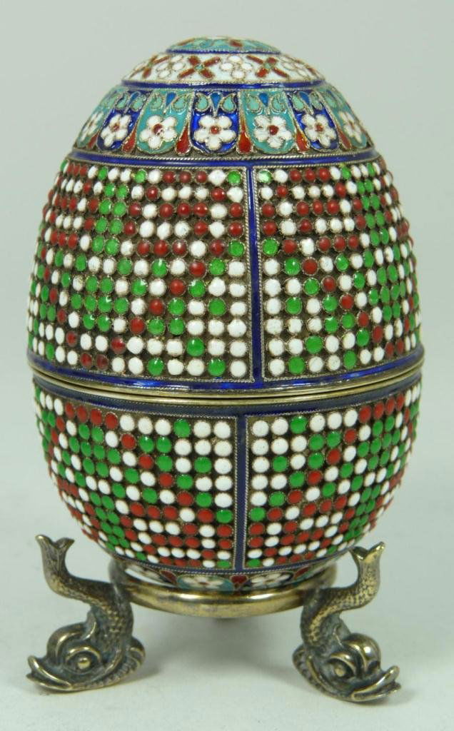 RUSSIAN SILVER ENAMELED BEADED EGG: Russian silver enameled egg box having multicolor beaded floral design throughout exterior. Hold round cabochon cut garnet jewel to bottom of egg. Gold wash interior. Includes stand with three figural