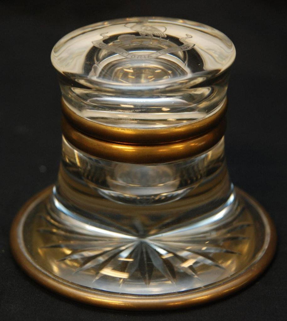ANTIQUE EUROPEAN GLASS AND BRASS INKWELL: Antique European brass and glass inkwell. Top has etched and frosted crest depicting a bird with crown standing on eggs with banner below holding the Latin saying 'AMAT- VICTORIA-CUPRAM' which transla