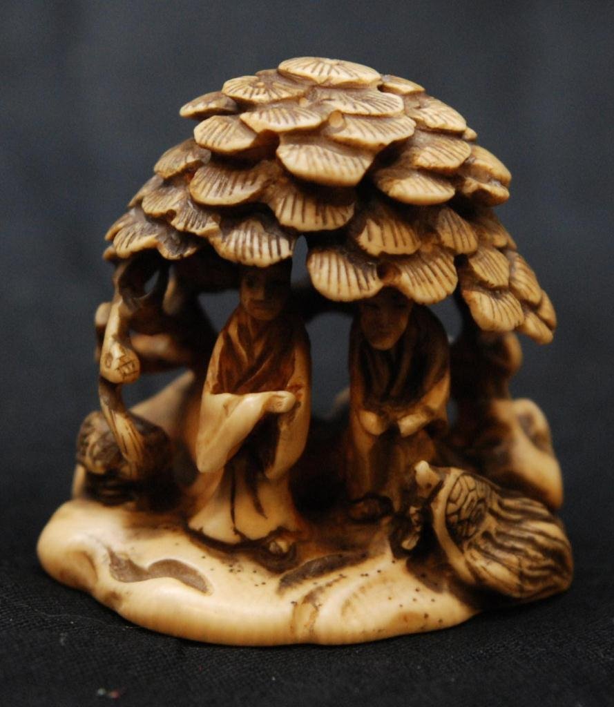 CHINESE CARVED IVORY NETSUKE OF COUPLE UNDER TREE: A Chinese fully relief carved ivory netsuke figure depicting a couple under a pine tree with crane and turtle. Signed to bottom. 19th/20th century. Measures 1 3/4" height x 1 3/4" width (4.4cm x 4.4cm
