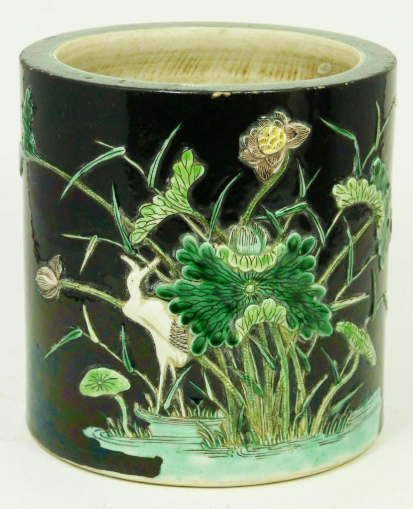 CHINESE KANGXI FAMILLE NOIR PORCELAIN BRUSH POT: An antique Chinese Famille Noir porcelain brush pot with raised pond scene over black ground. Etruscan pattern border to rim. Impressed Kangxi period (1662-1722) Artemisia leaf mark to bottom. Measure