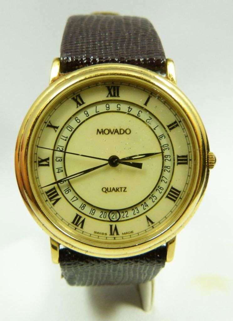 MEN'S MOVADO GOLD PLATE DRESS WATCH: Gent's Movado gold plate dress watch. Has ivory enameled face with gold hour, minute and second hands. Has rotating date design. Gold Roman numeral numbering. Lizard leather band. Includes original bo