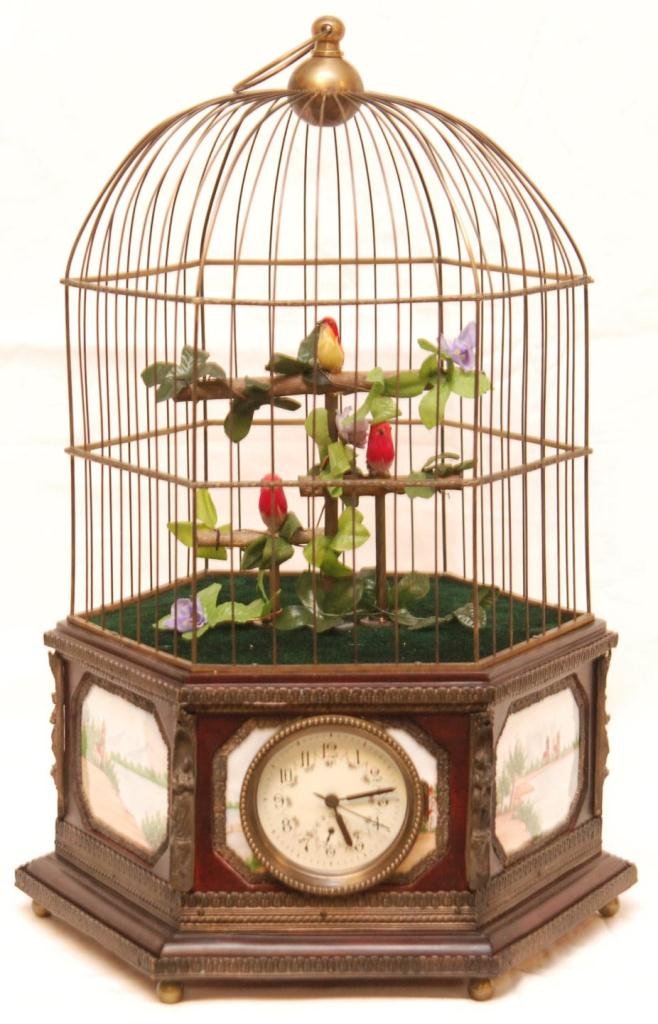 ANIMATED SINGING BIRD CAGE BRASS MUSIC BOX & CLOCK: Old German figural singing bird cage having hexagonal shape with hand painted enamel plaques to each side depicting landscape scenes with cathedrals. Has clock mounted to front of cage. Mid 20th centu