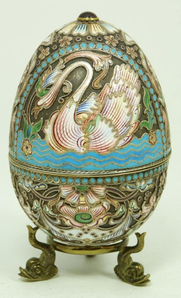 RUSSIAN SILVER JEWELED & ENAMELED EGG BOX: Russian silver enameled and jeweled egg box with elegant multicolor design depicting swans. Round cabochon cut rubies set on top and bottom. Gold wash interior. Includes stand with three figural fish
