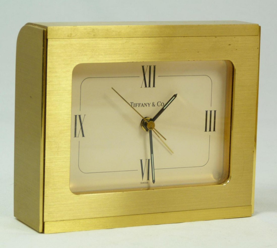 TIFFANY & COMPANY BRASS DESK SWISS ALARM CLOCK: Tiffany & Company brass desk alarm clock having a cream face with Roman numerals. Black hour and minute hand with gold second and alarm hand. Gold tone throughout. Original Tiffany & Co. Swiss quartz 