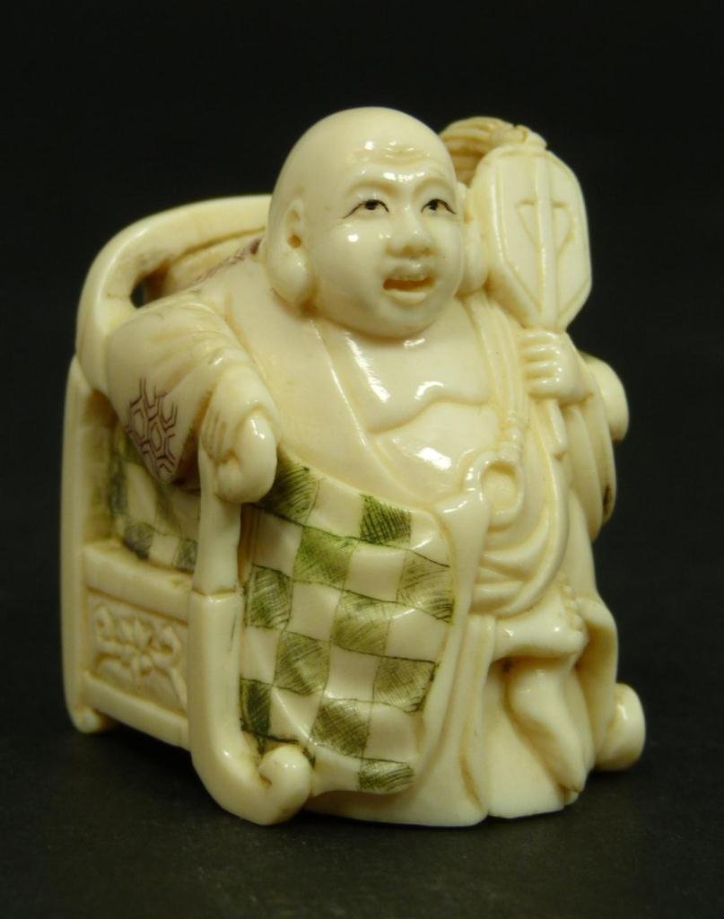 POLYCHROMED & CARVED IVORY NETSUKE OF BUDDHA: Japanese carved and polychromed depiction of Hotei Buddha on throne. Black enameled eyes. Signed on bottom. Meiji to Showa period. Measures 1 7/8 inch height (4.7 cm). Total weight of 34 grams.