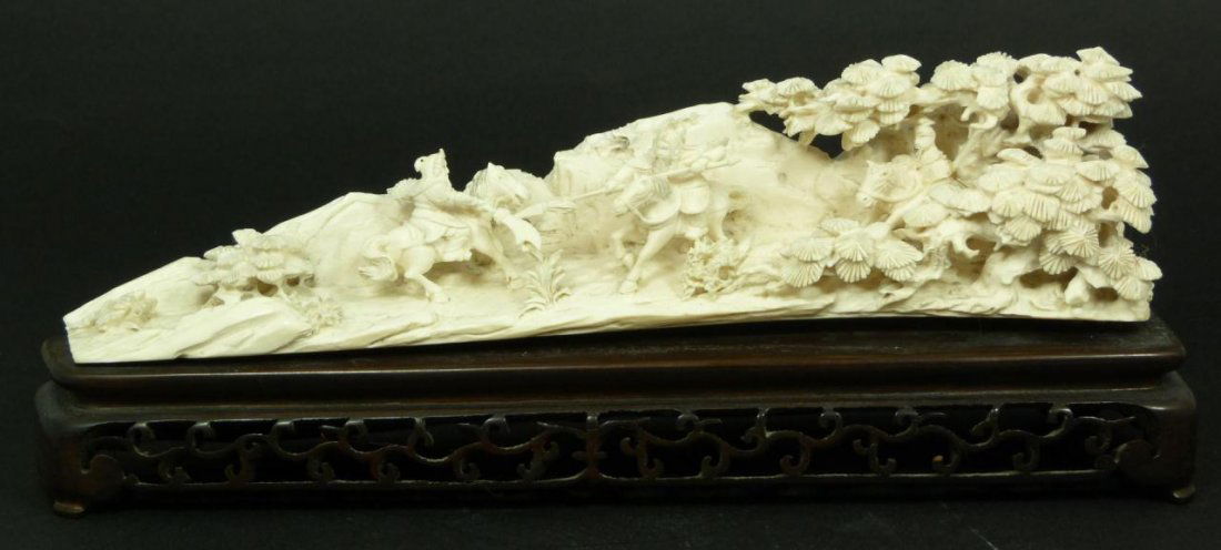 CARVED CULTURAL REVOLUTION IVORY BATTLE SCENE TUSK: A fully relief carved Chinese ivory battle scene tusk depicting a warrior battle scene. To the right hand side another warrior is standing under pine trees and observing the battle. Rock formations se