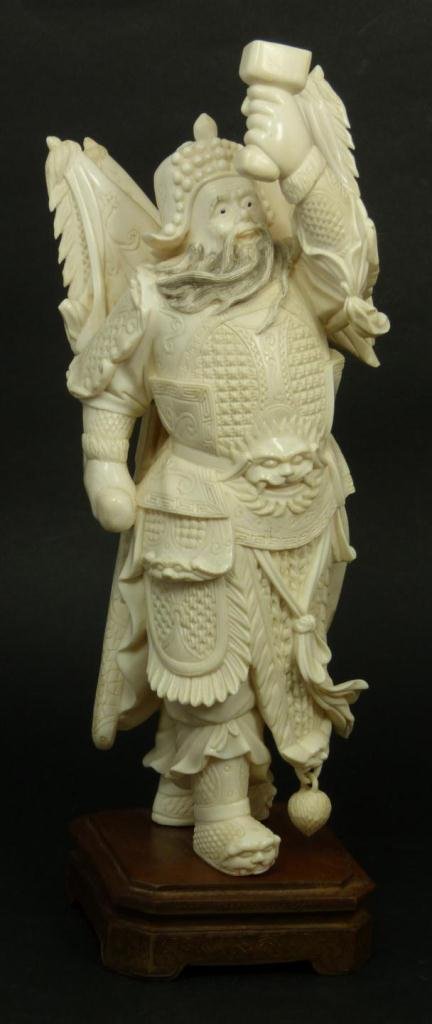 CHINESE CARVED IVORY MALE WARRIOR FIGURE: A finely carved Chinese ivory sculpture depicting a standing male warrior holding sword up with left hand. Black enameled eyes. Mounted on wooden base. Height Measures 9 7/8in Height + 1 1/8in Base He