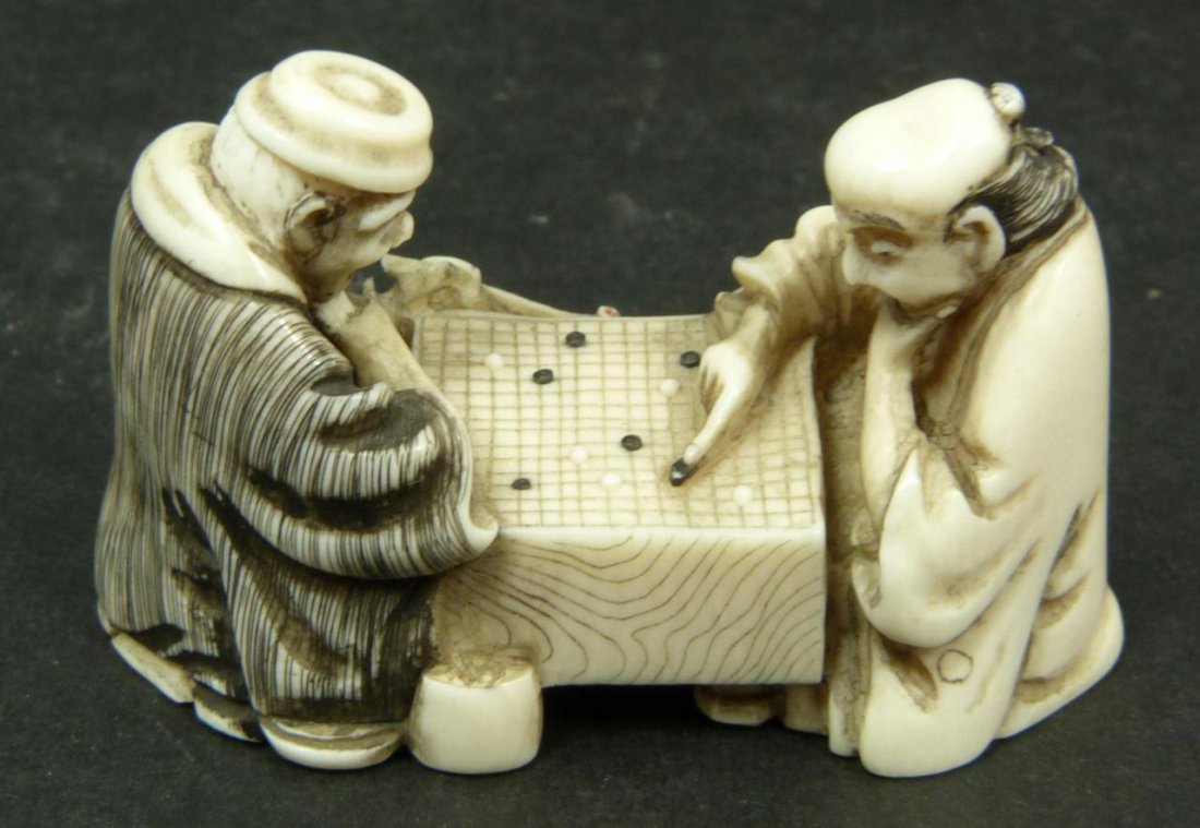 JAPANESE CARVED IVORY NETSUKE OF GAME SCENE: A Japanese carved ivory netsuke scene depicting two men playing games of go. Etched calligraphy signature to bottom. Measures 1. 1/4in Height x 1 7/8in Width. Weighs 17g.