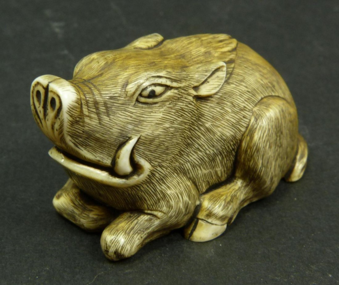 JAPANESE CARVED IVORY NETSUKE OF BOAR: Japanese carved netsuke figure depicting a recumbent boar. Signed to inlaid plaque. Measures 1 1/8in Height x 2in Length. Weighs 27g.