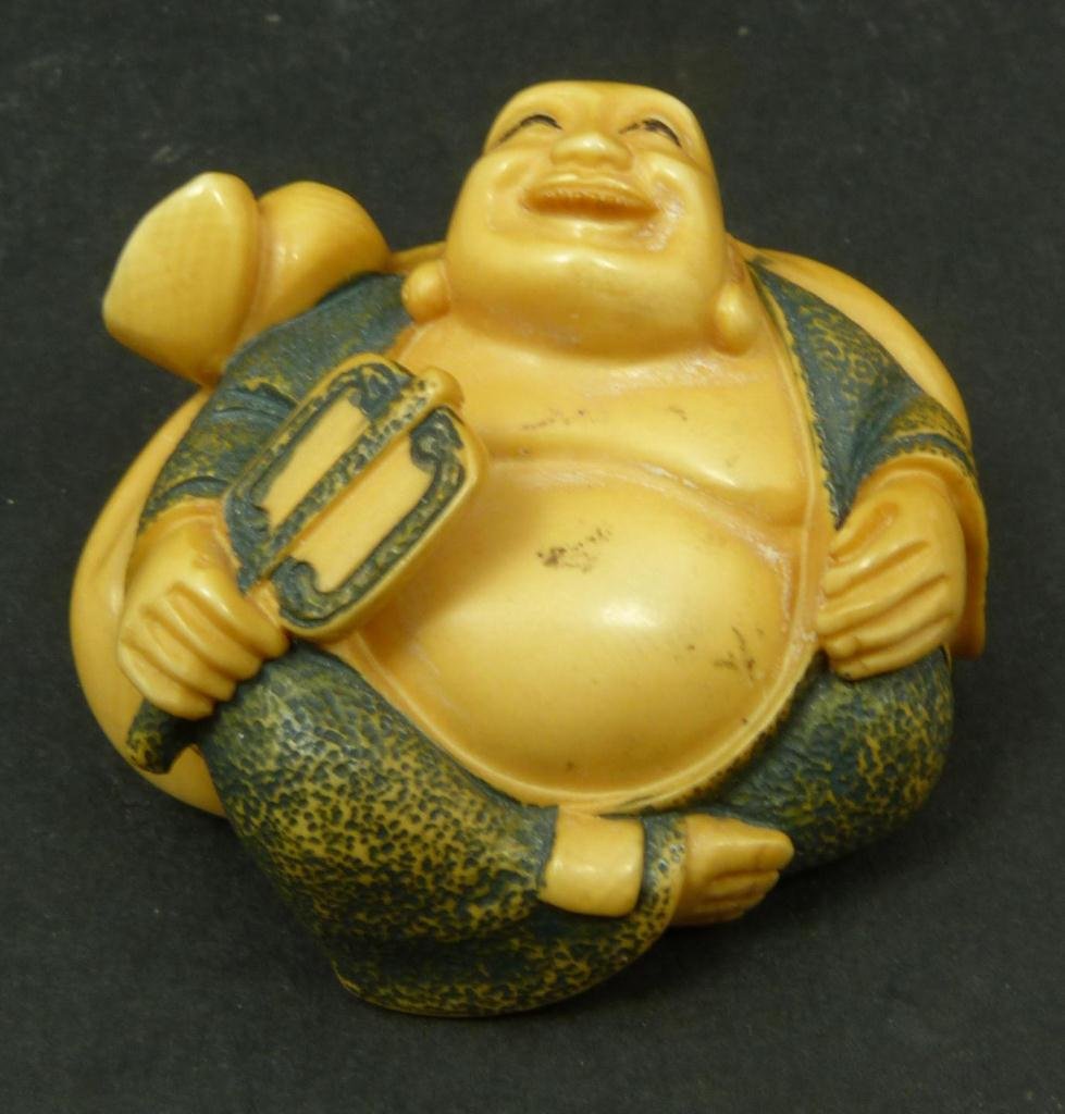 JAPANESE CARVED IVORY BUDDHA NETSUKE FIGURE: Japanese hand carved and polychromed ivory Netsuke figure depicting seated and happy Hotie Buddha. Etched calligraphy to bottom. Measures 1 3/8in Height x 2in Width. Weighs 47g.