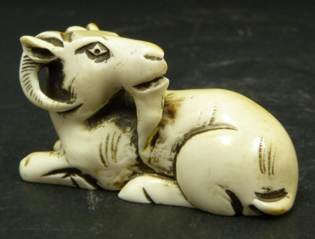 JAPANESE CARVED IVORY NETSUKE OF RAM FIGURE: Japanese carved ivory figure depicting a recumbent ram with feet tucked to side. Etched calligraphy signature to bottom. Measures 1 1/8in Height x 2in Length. Weighs 21g.