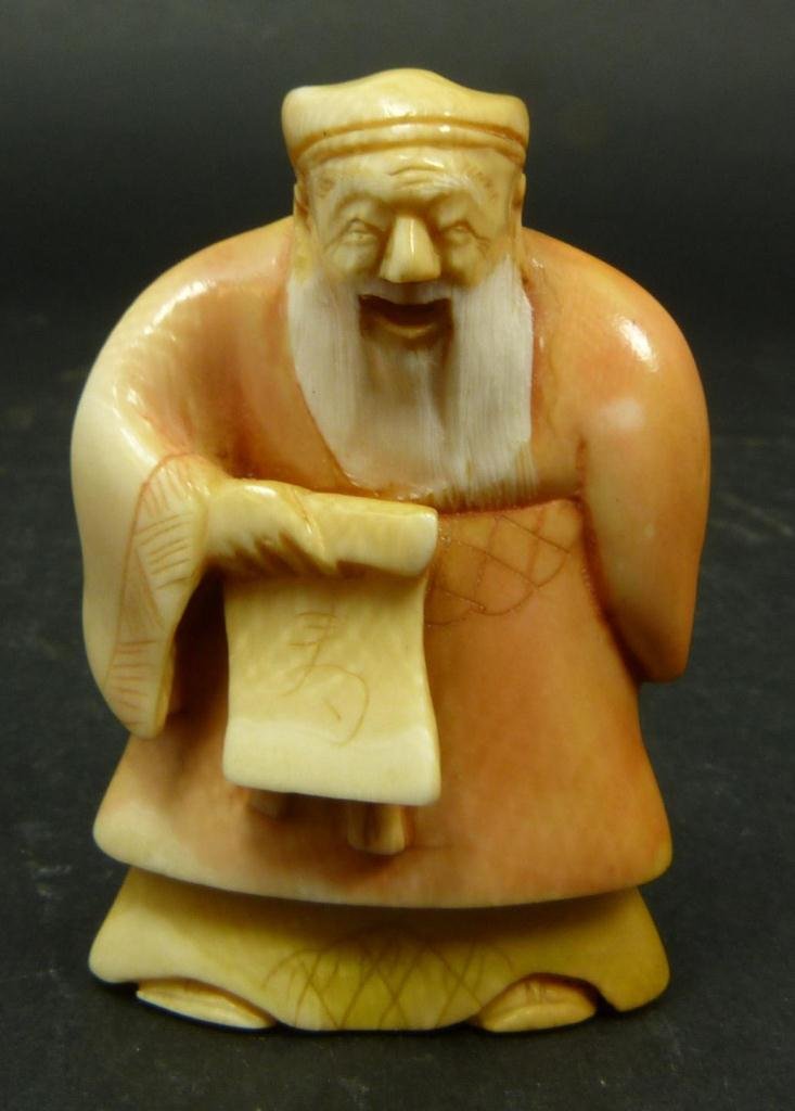 JAPANESE CARVED IVORY NETSUKE OF WISEMAN: Japanese carved and polychromed ivory netsuke figure depicting Wiseman with scroll. Etched calligraphy signature to bottom. Measures 2 1/8in Height. Weighs 35g