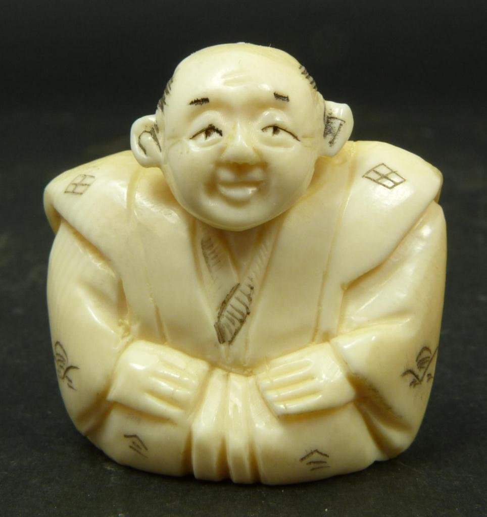 JAPANESE CARVED IVORY NETSUKE OF SEATED MAN: Japanese carved ivory netsuke depicting seated man. Etched calligraphy signature to bottom. Measures 1 3/8in Height. Weighs 17g.