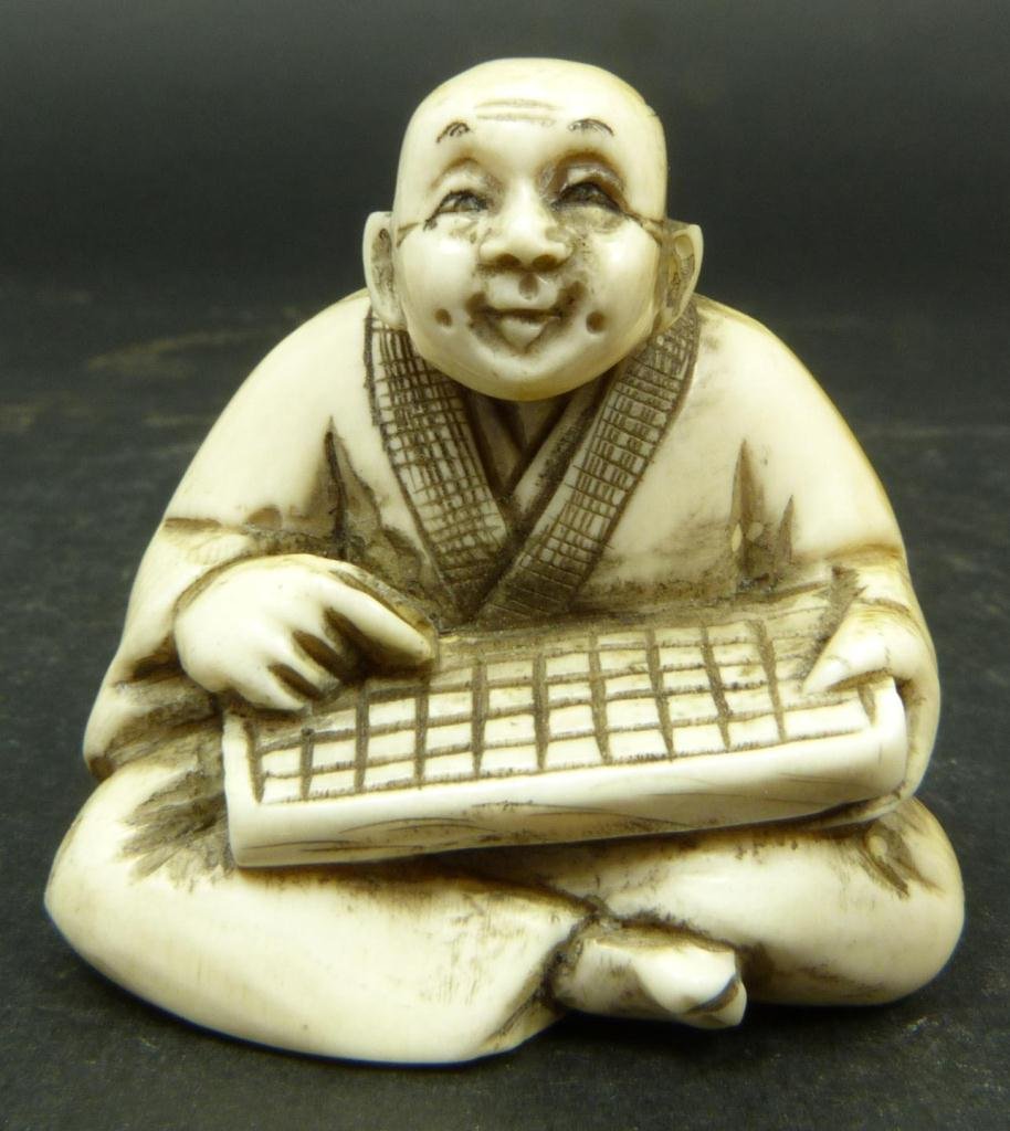 JAPANESE CARVED IVORY NETSUKE FIGURE OF MAN: Japanese hand carved ivory netsuke figure depicting a seated man with abacus. Etched calligraphy signature to bottom. Measures 1/2in Height. Weighs 25 grams.