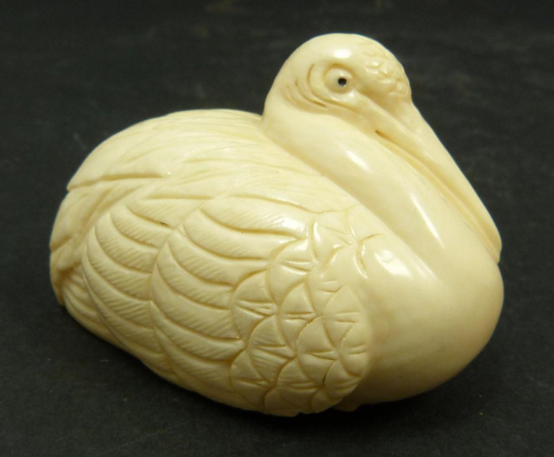 JAPANESE CARVED IVORY CRANE NETSUKE: Japanese carved ivory netsuke figure depicting a recumbent crane. Etched calligraphy signature to bottom. Measures 1/25in Height x 2 1/8in Length. Weighs 36g.