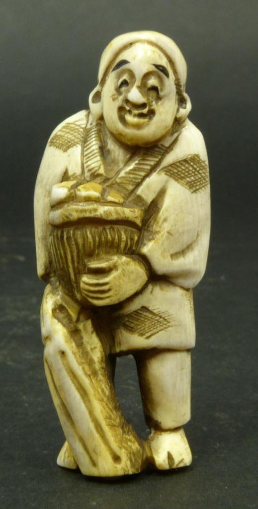 JAPANESE CARVED IVORY NETSUKE OF FRUIT MERCHANT: Japanese carved ivory netsuke figure depicting merchant with fruit basket. Etched calligraphy signature to bottom. Measures 2.5in Height. Weighs 21g.