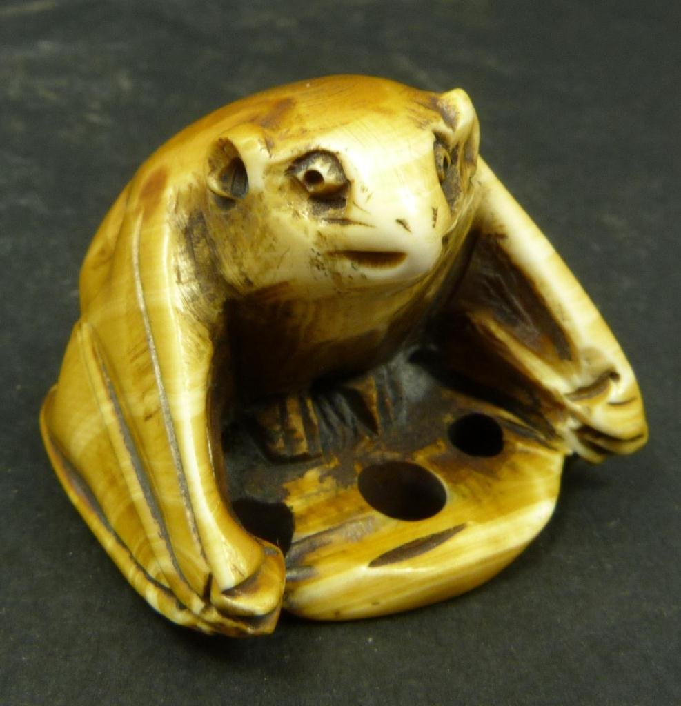 JAPANESE CARVED IVORY NETSUKE OF BAT: Japanese carved tea stained ivory netsuke depicting a bat. Etched calligraphy signature to bottom. Measures 1 3/8in Height x 1 7/8in Length. Weighs 29g.