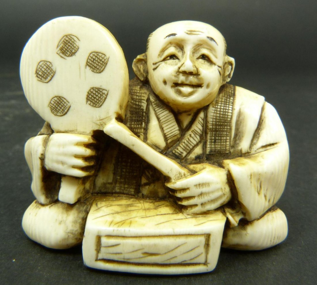 JAPANESE CARVED IVORY NETSUKE OF MAN WITH PADDLE: Japanese carved ivory netsuke figure depicting a seated man holding a paddle to right hand. Etched calligraphy signature to bottom. Measures 1 7/8in Width. Weighs 27g.
