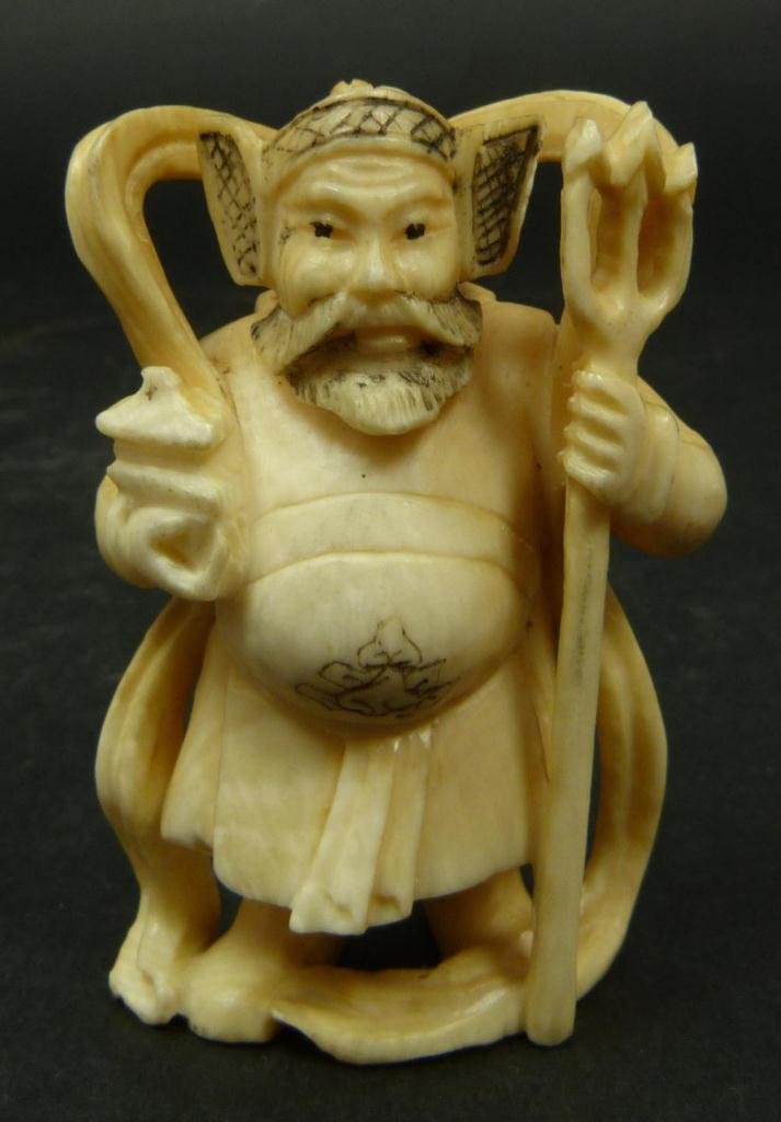 JAPANESE CARVED IVORY NETSUKE FIGURE OF WARRIOR: Japanese carved ivory netsuke depicting a standing warrior with trident. Etched calligraphy signature to bottom. Measures 1 1/8in Height. Weighs 25g.