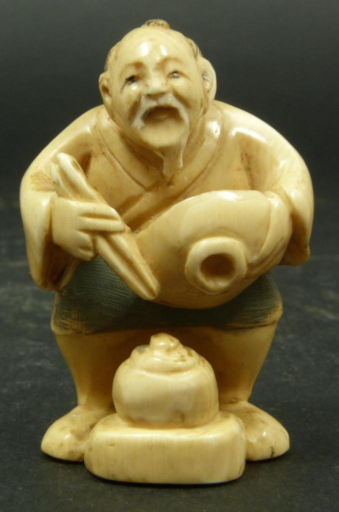 JAPANESE CARVED IVORY NETSUKE FIGURE OF MAN EATING: Japanese carved ivory netsuke figure depicting a standing man holding bowl and chop sticks with a pot of rice at his feet. Etched calligraphy signature to bottom. Measure 2in Height. Weighs 23g.