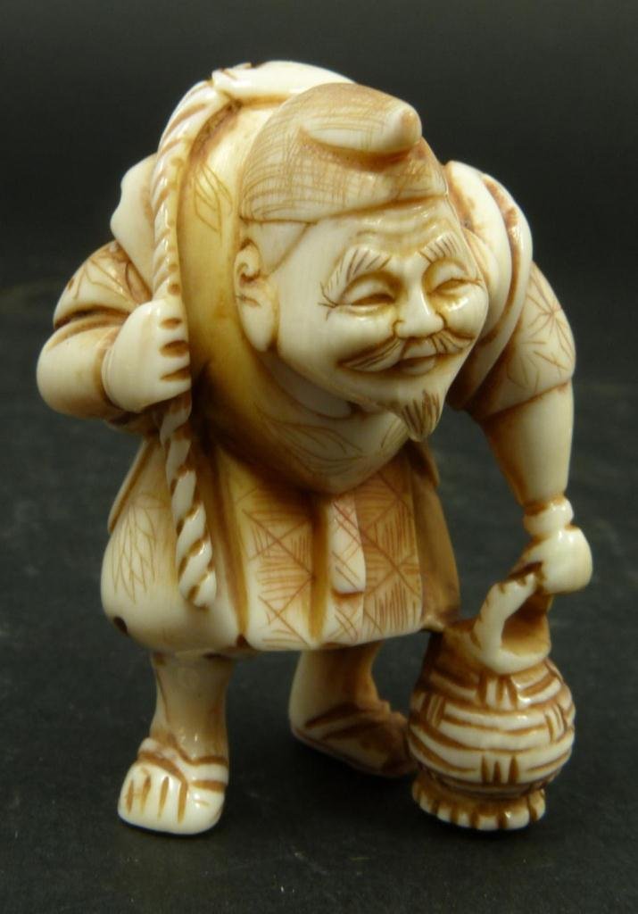 JAPANESE CARVED IVORY NETSUKE OF FISHERMAN: Japanese hand carved tea stain ivory netsuke figure depicting fisherman with fish on back. Etched calligraphy to bottom. Measures 2in Height. Weighs 35g.