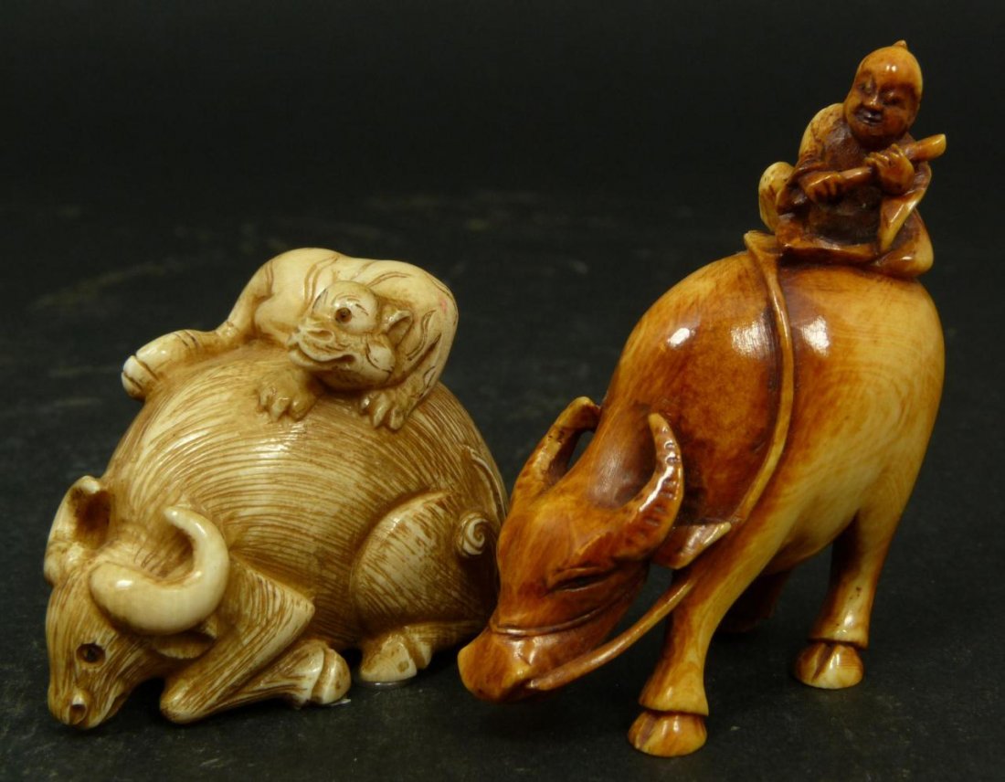 2 JAPANESE CARVED IVORY NETSUKE OX FIGURES: Lot of two Japanese carved Ivory Netsuke group figures depicting an ox with tiger on back, and ox with child on back. Measures 2 1/8in Height. Total Weight 59g.