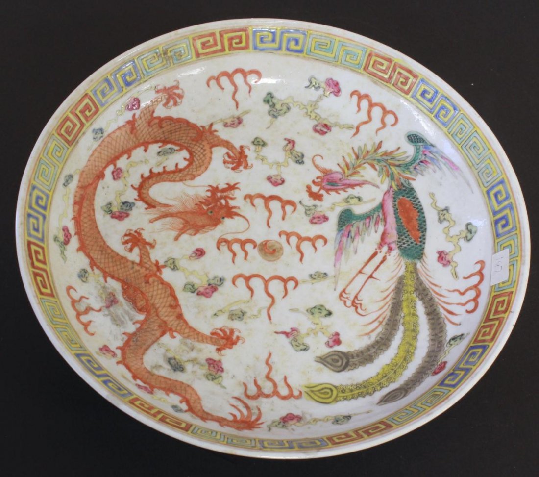 CHINESE PORCELAIN HAND PAINTED ENAMELED DISH: An antique Chinese hand painted enameled wide coupe bowl depicting multicolor dragon and phoenix amongst lingzhi form clouds and flames with pearl. Etruscan pattern to rim. Peony blooms and vines to e