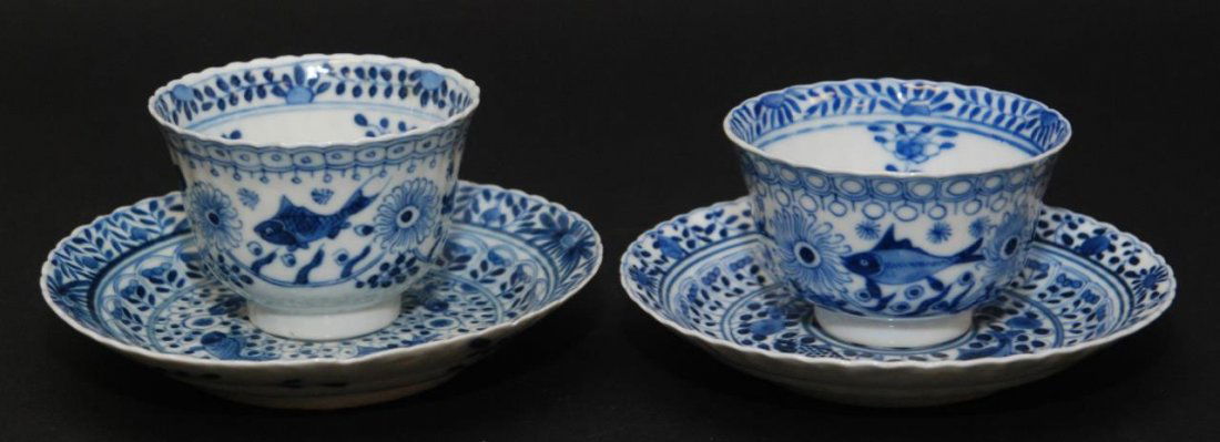 Pr CHINESE PORCELAIN KANGXI TEACUPS w SAUCERS: A pair of Chinese hand painted blue and white porcelain tea cups, each having a fish and flower design to exterior. Each holding blue four character Kangxi (1662-1722) reign marks. Cups measure approx