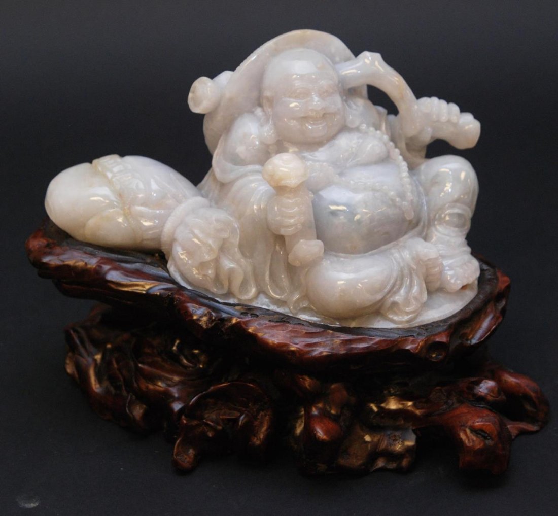 CHINESE CARVED WHITE JADE BUDDHA SCULPTURE: Chinese hand carved white jadeite sculpture depicting a seated Hotei Buddha holding lingzhi scepter. Includes fitted wooden base. Glowing mottled white jade with light pale green colors and hints of r