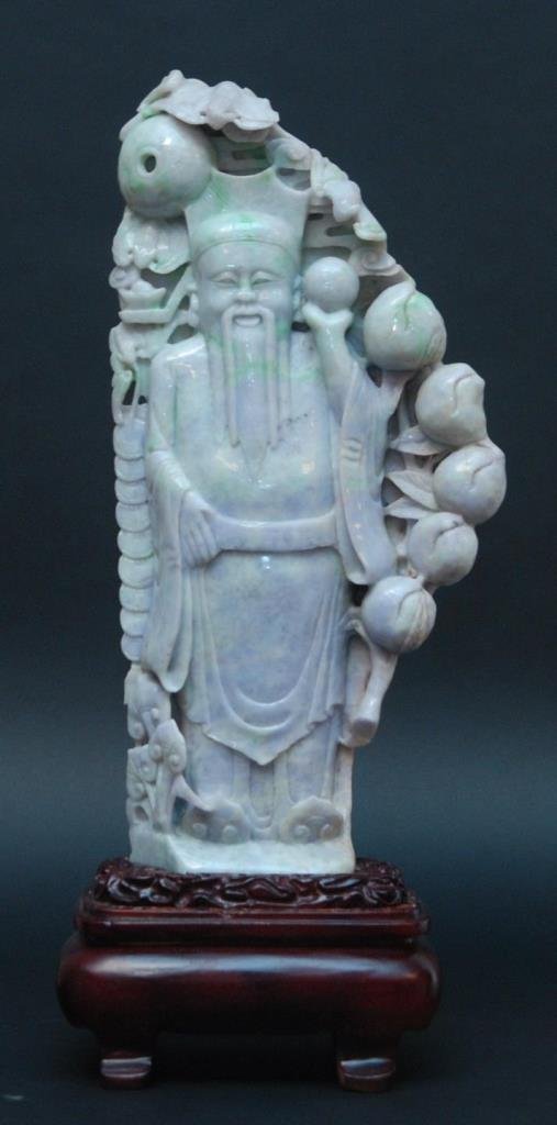CHINESE LAVENDER & APPLE GREEN JADEITE SCULPTURE: A large Chinese hand carved lavender and apple green jadeite sculpture depicting a standing Shou Xing surrounded by bats, peaches, coins and lingzhi. Glowing mottled lavender and apple green jade colo