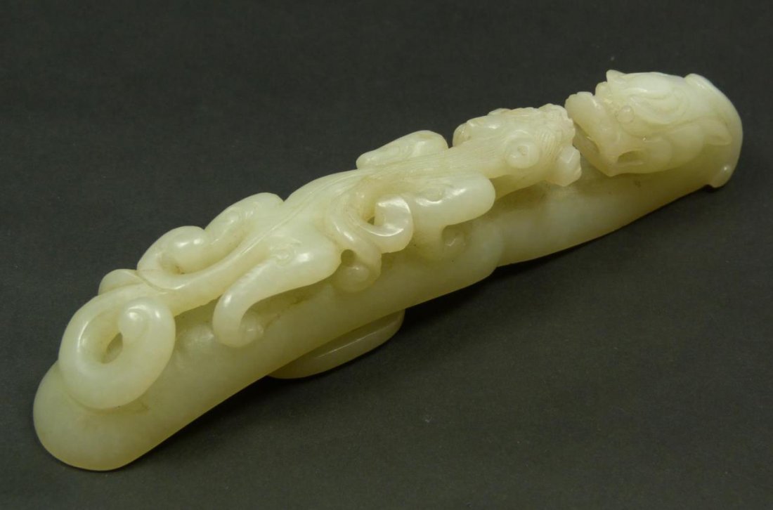RARE CARVED MUTTON FAT JADE RUYI GARMENT HOOK: A rare and finely carved white mutton fat jade garment hook. Has a figural Chih lung dragons design in ruyi scepter form. Translucent pale green to white mottled jade. Measures 5 1/2" length (13.9cm).