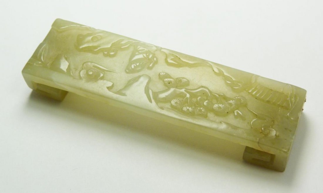 CHINESE RELIEF CARVED JADE INK BED: A Chinese relief carved jade ink bed depicting a scholar on a mountain trail with pine trees, rock formations and bridges. Glowing translucent even toned white jade color. Measures 3 1/2" length x 1" 