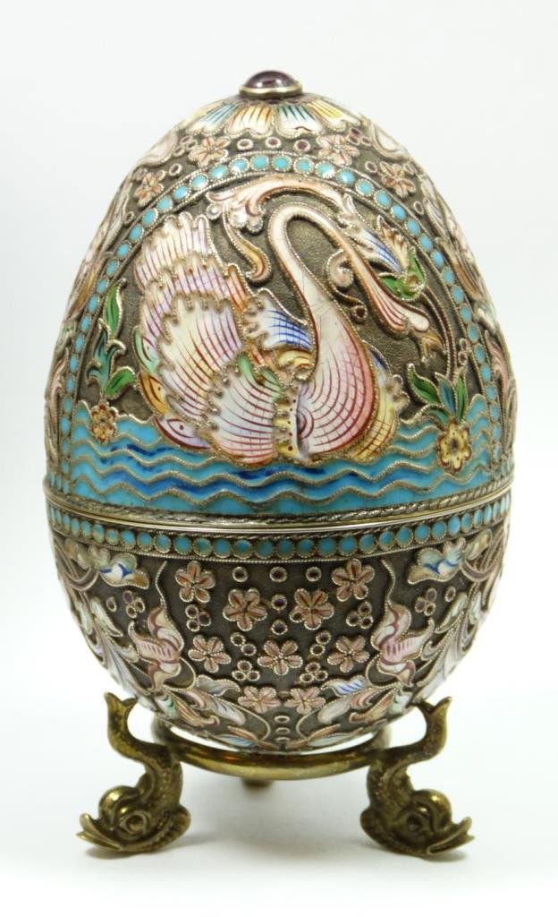 RUSSIAN SILVER JEWELED & ENAMELED EGG BOX: Russian silver enameled and jeweled egg box with elegant multicolor design depicting swans. Round cabochon cut rubies set on top and bottom. Gold wash interior. Includes stand with three figural fish