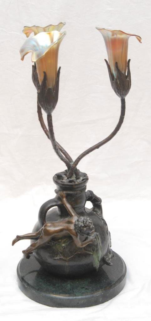 BRONZE & GLASS AMPHORA LAMP AFTER AGUSTE MOREAU: A bronze lamp depicting an amphora vase with cherub. Extending from the vase is three flora form stems completed with Tiffany Aurene style shades. Signed Auguste Moreau to side of lamp. After Auguste
