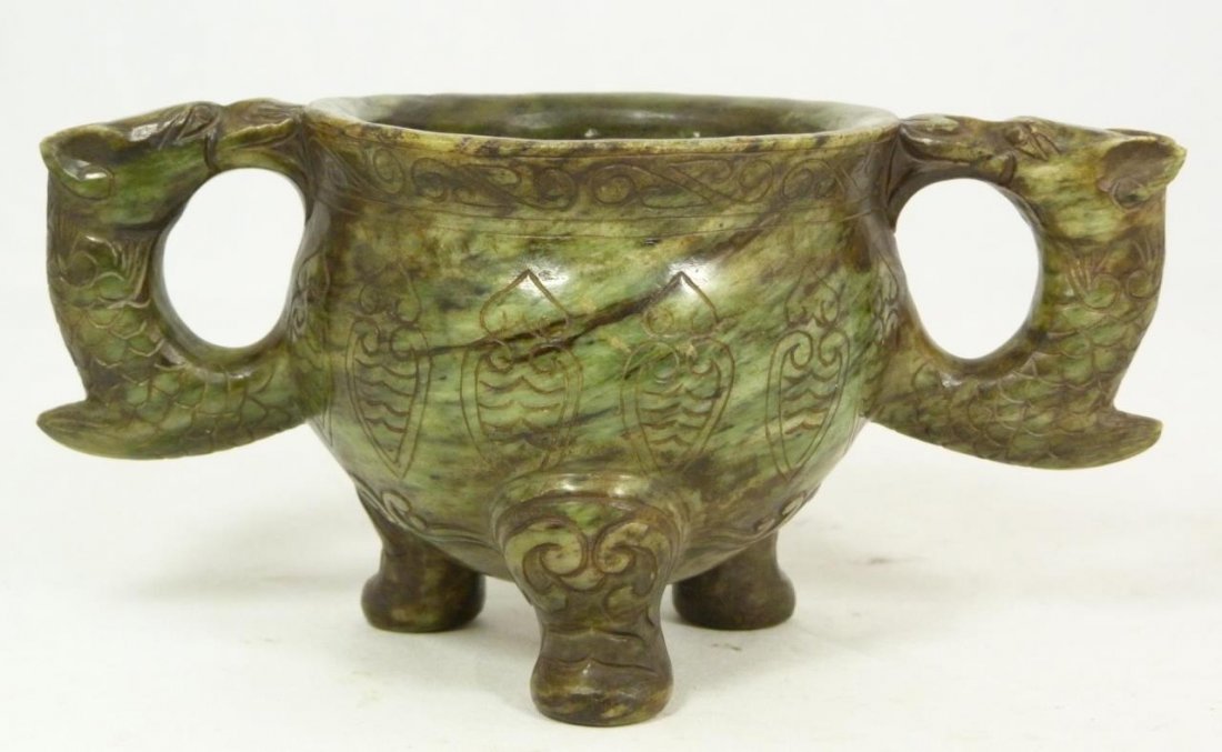 CHINESE CARVED ARCHAIC JADE HANDLED CUP: Chinese hand carved jade archaic style handled tripod cup. Figural dragon handles to sides. Etched lingzhi designs to side of body. 19th/20th century. Measures 3 1/2" height x 7 5/8" width (8.9cm x 19