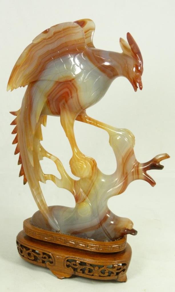 CHINESE CARNELIAN CARVED PHOENIX BIRD ON BASE: A Chinese hand carved carnelian stone figure depicting a perched phoenix bird on branch. Includes fitted wooden reticulated base. Measures 8 1/4" height + 1 3/4" base height (20.9cm + 4.4cm). Total we